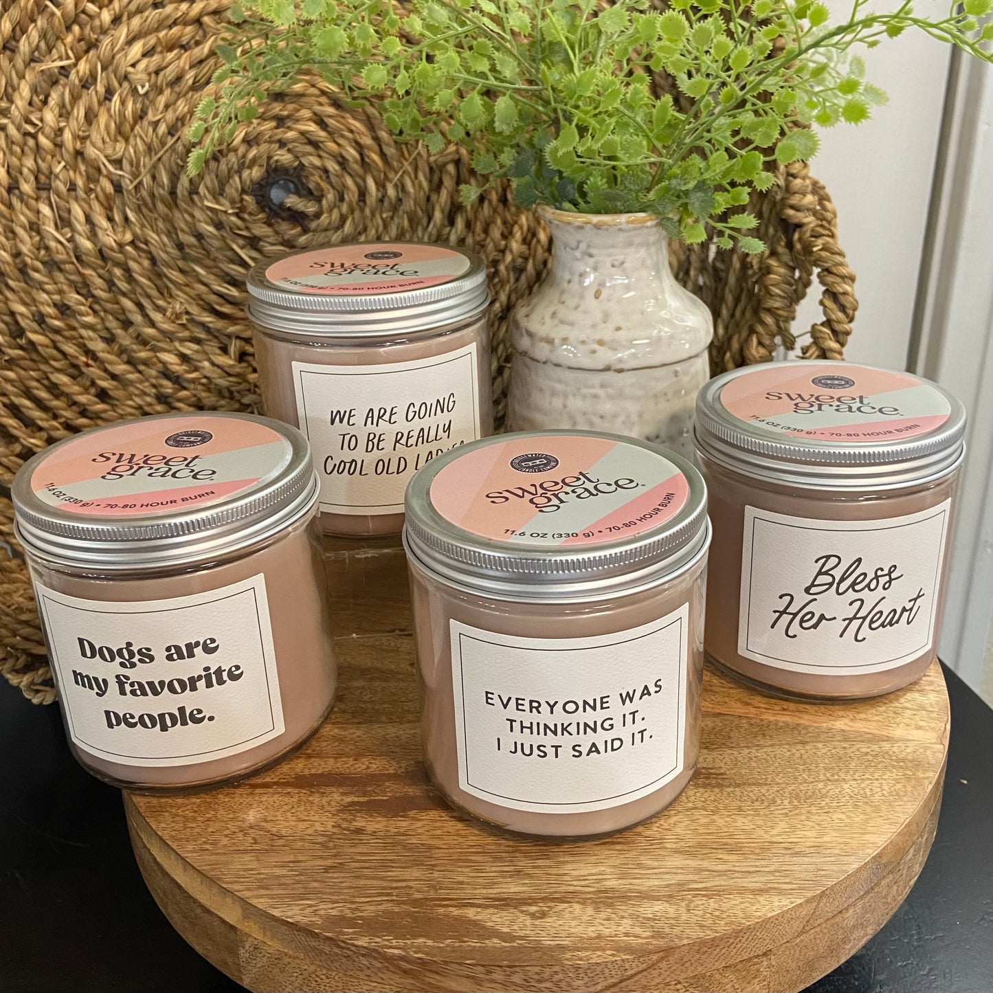 Five candles with humorous labels on a wooden surface, surrounded by decorative elements.