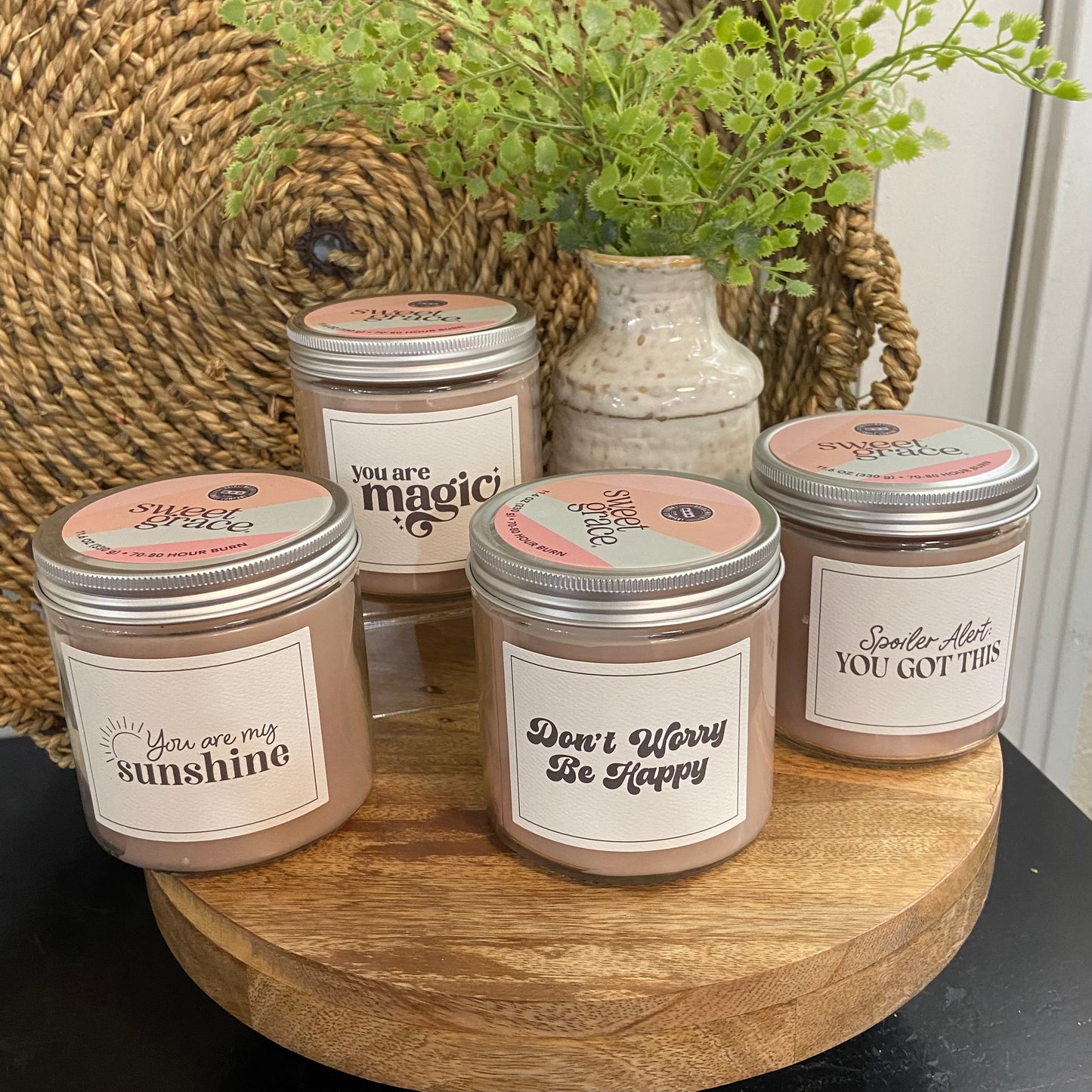 Five candles with motivational labels on a wooden stand with a plant in the background.