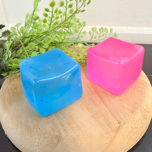 Blue and pink square containers on a wooden surface with greenery in the background