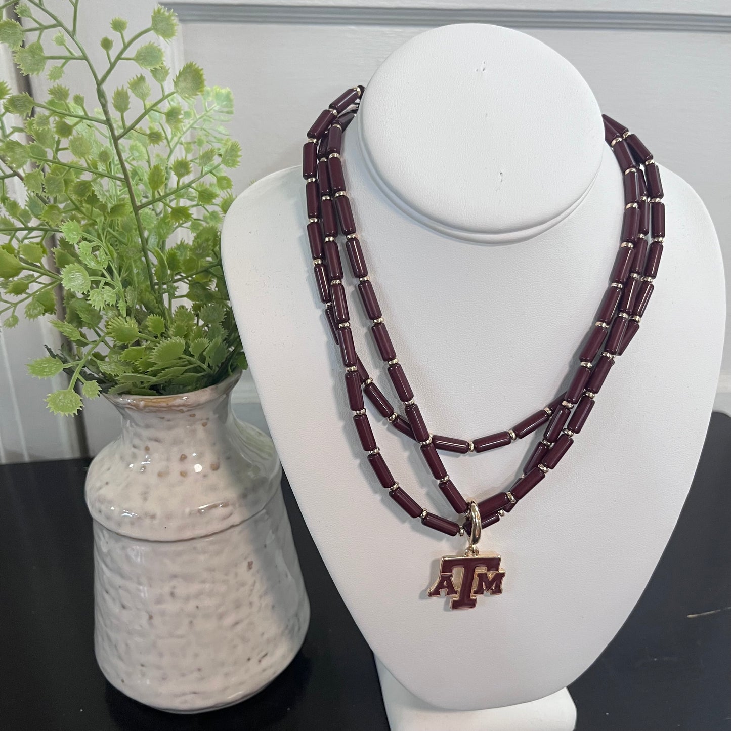Beaded necklace with a pendant on a mannequin bust next to a vase with greenery.