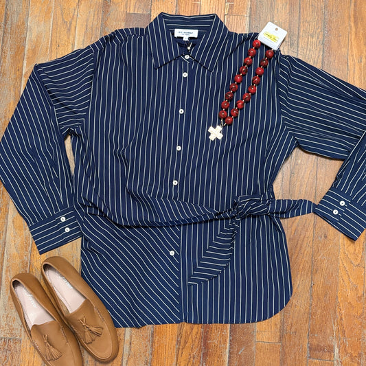 A navy blue long-sleeve button-up shirt with thin white vertical pinstripes, styled in a flat lay on a wooden floor with a brown tassel loafer and a red beaded necklace.