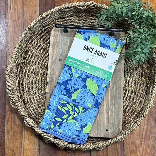 Blue floral towel with packaging on a wooden tray with a woven basket and greenery.