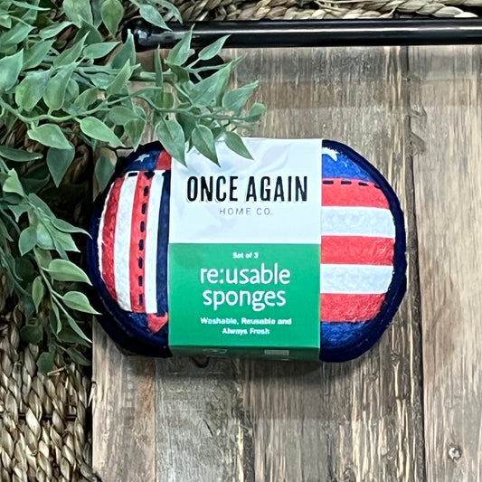 Pack of reusable sponges with American flag design on a wooden surface with greenery.