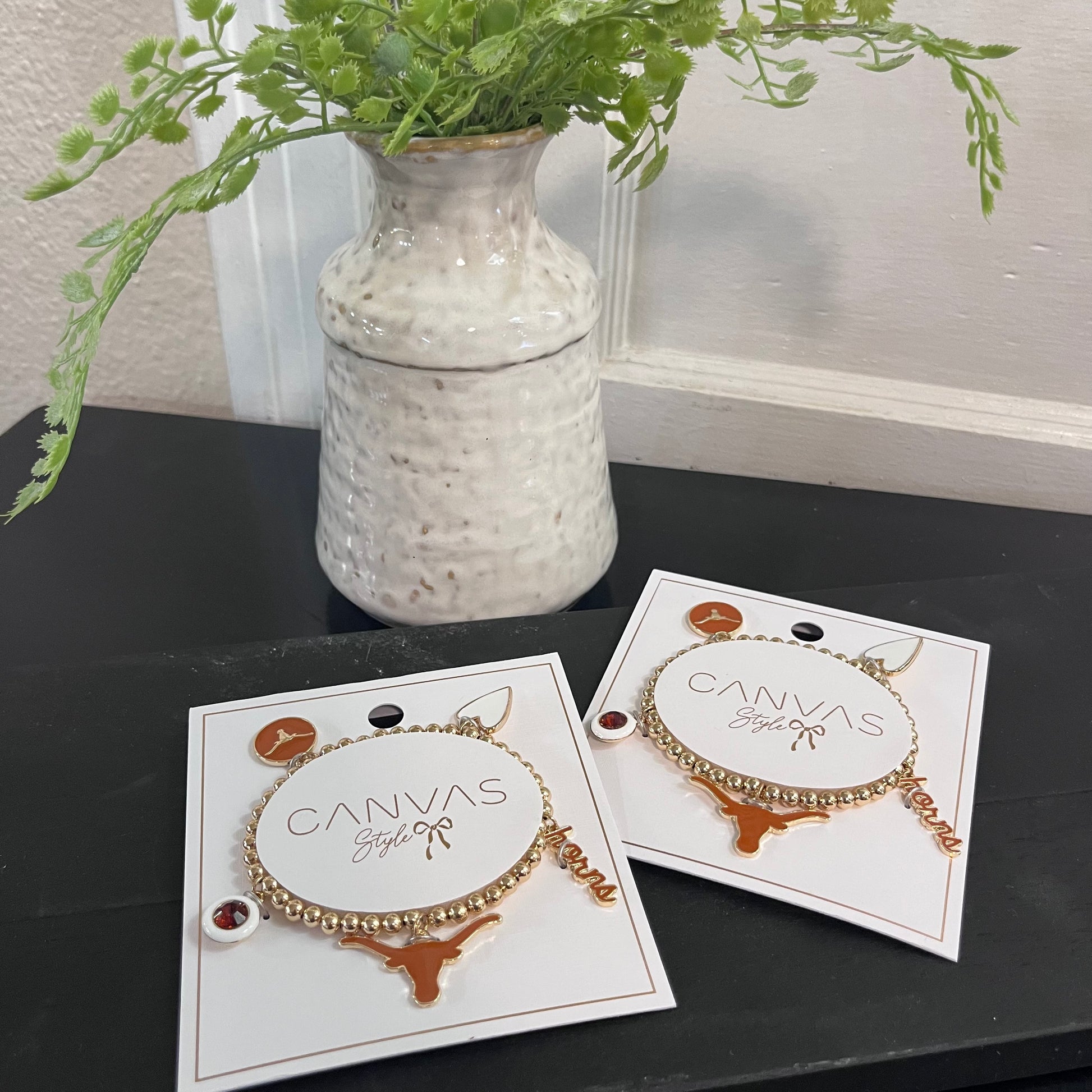 Two bracelets on display cards with a vase of greenery in the background.