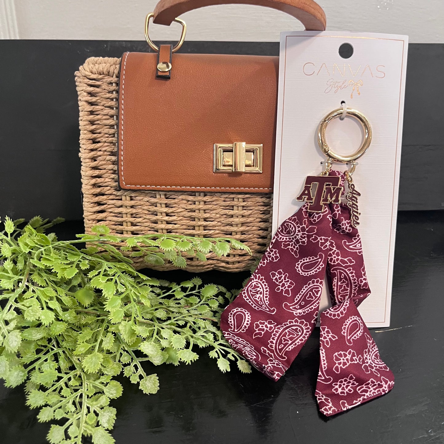 Woven handbag with a keychain and plant on a dark surface