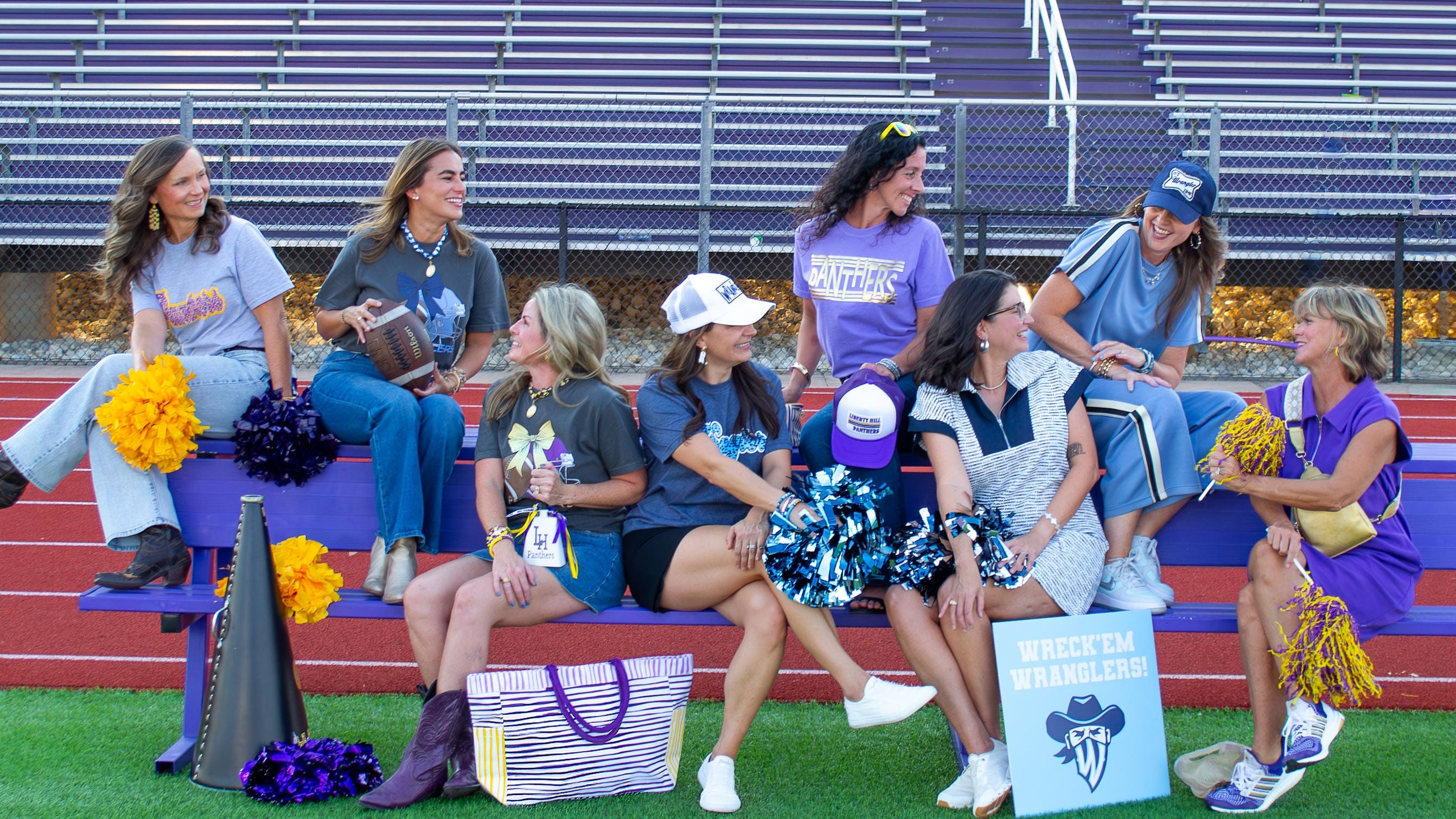 Teachers sitting on bleachers with sports equipment and promotional items on a football field.
