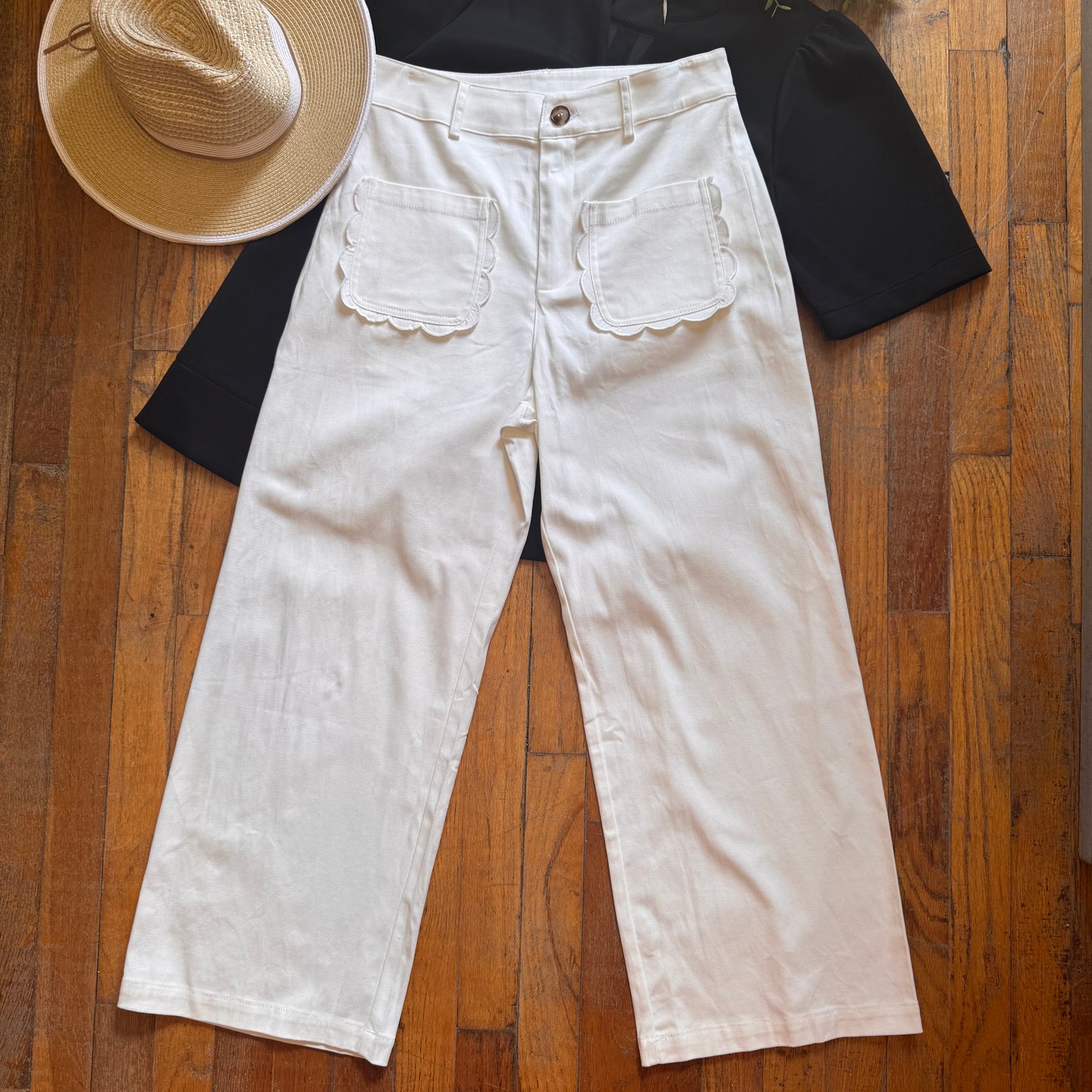 White wide-leg jeans with a black shirt and straw hat on a wooden floor
