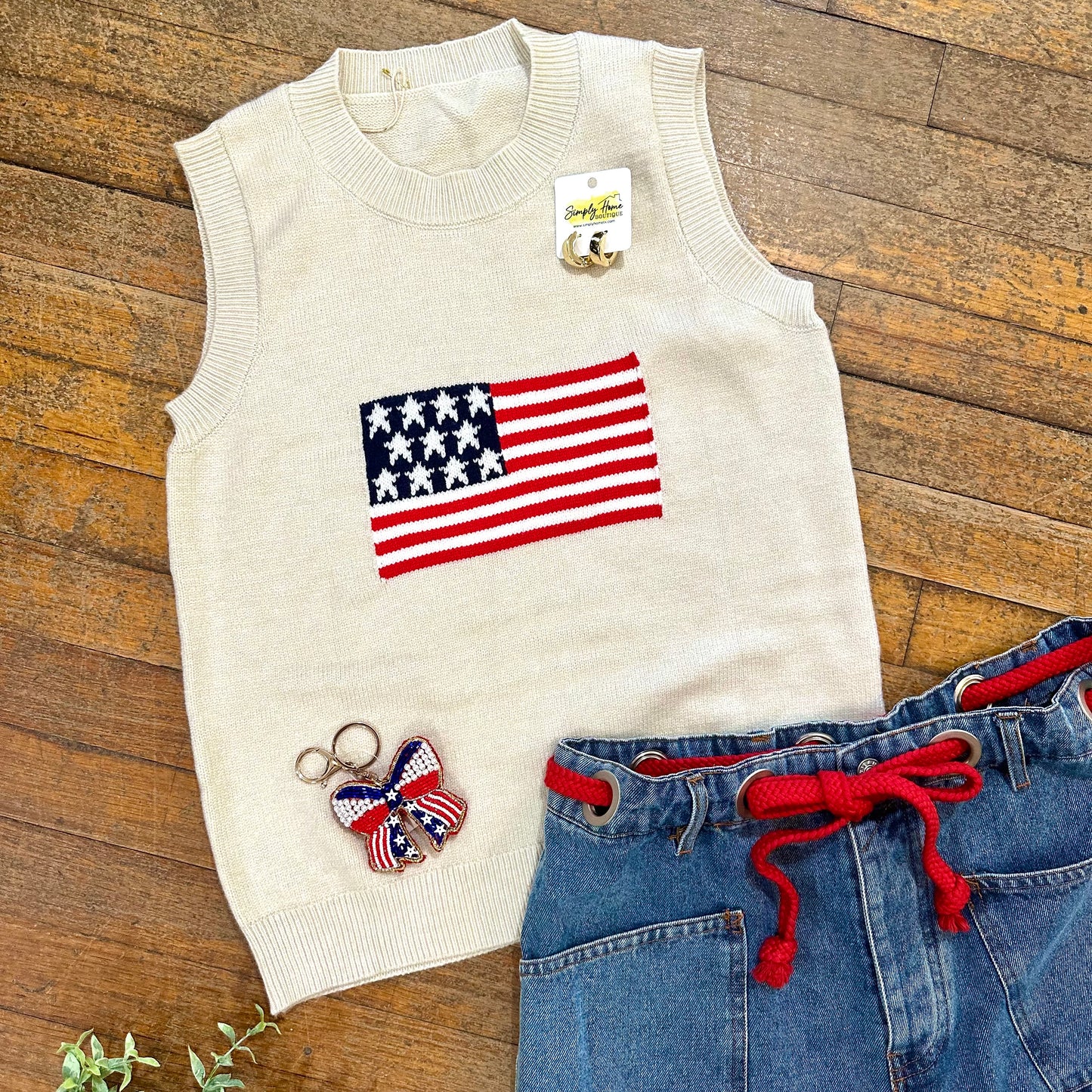 White sleeveless sweater with American flag design, blue jeans, and butterfly keychain on wooden surface