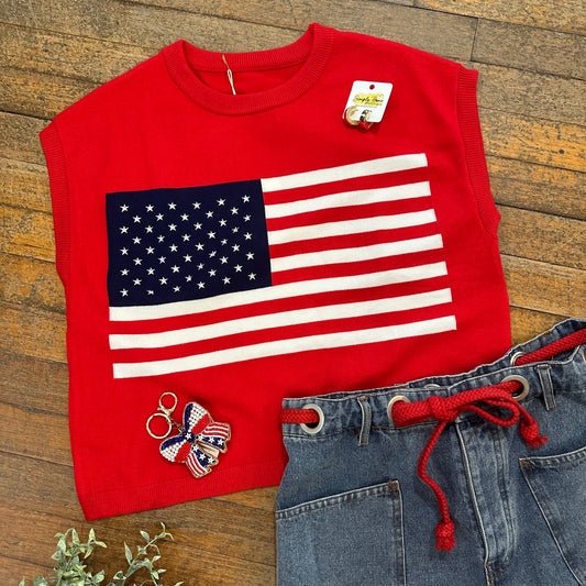 Red sleeveless top with American flag design, blue jeans, and decorative keychain on wooden surface