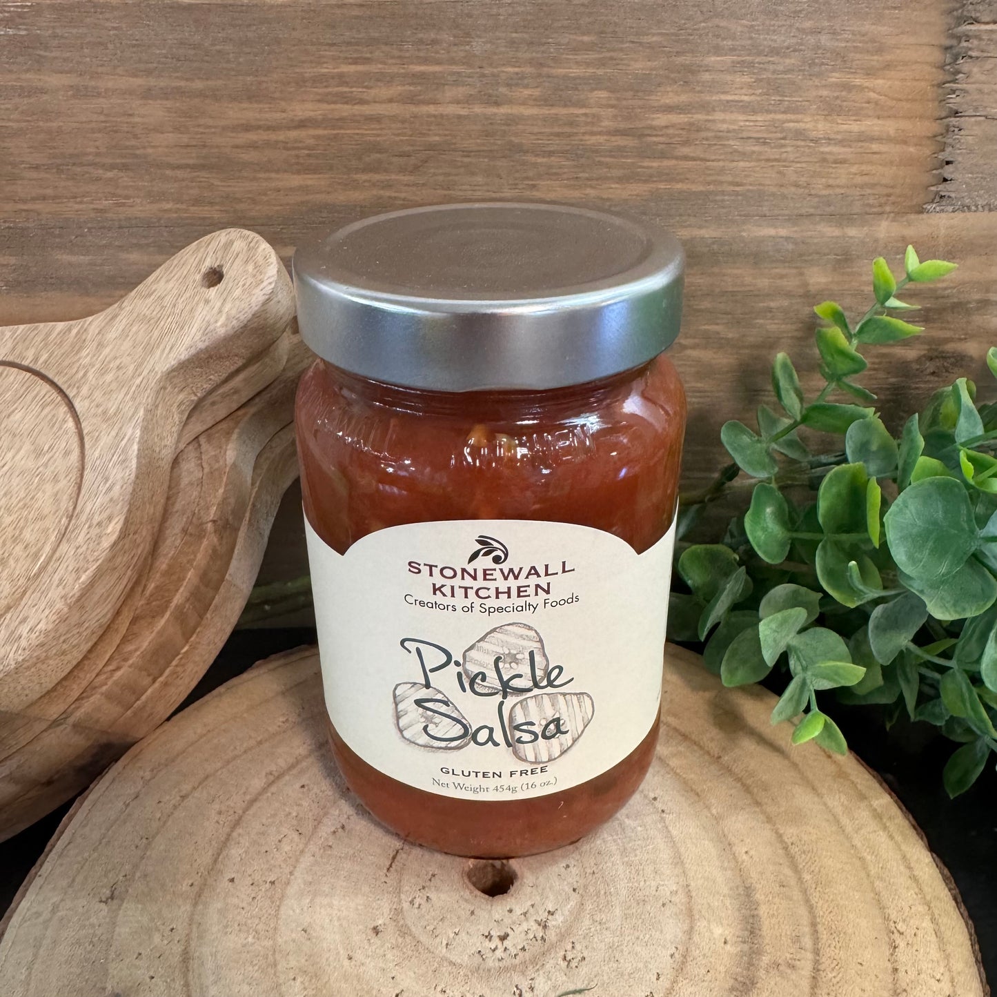 Jar of Stonewall Kitchen Pickle Salsa on a wooden surface with a plant in the background
